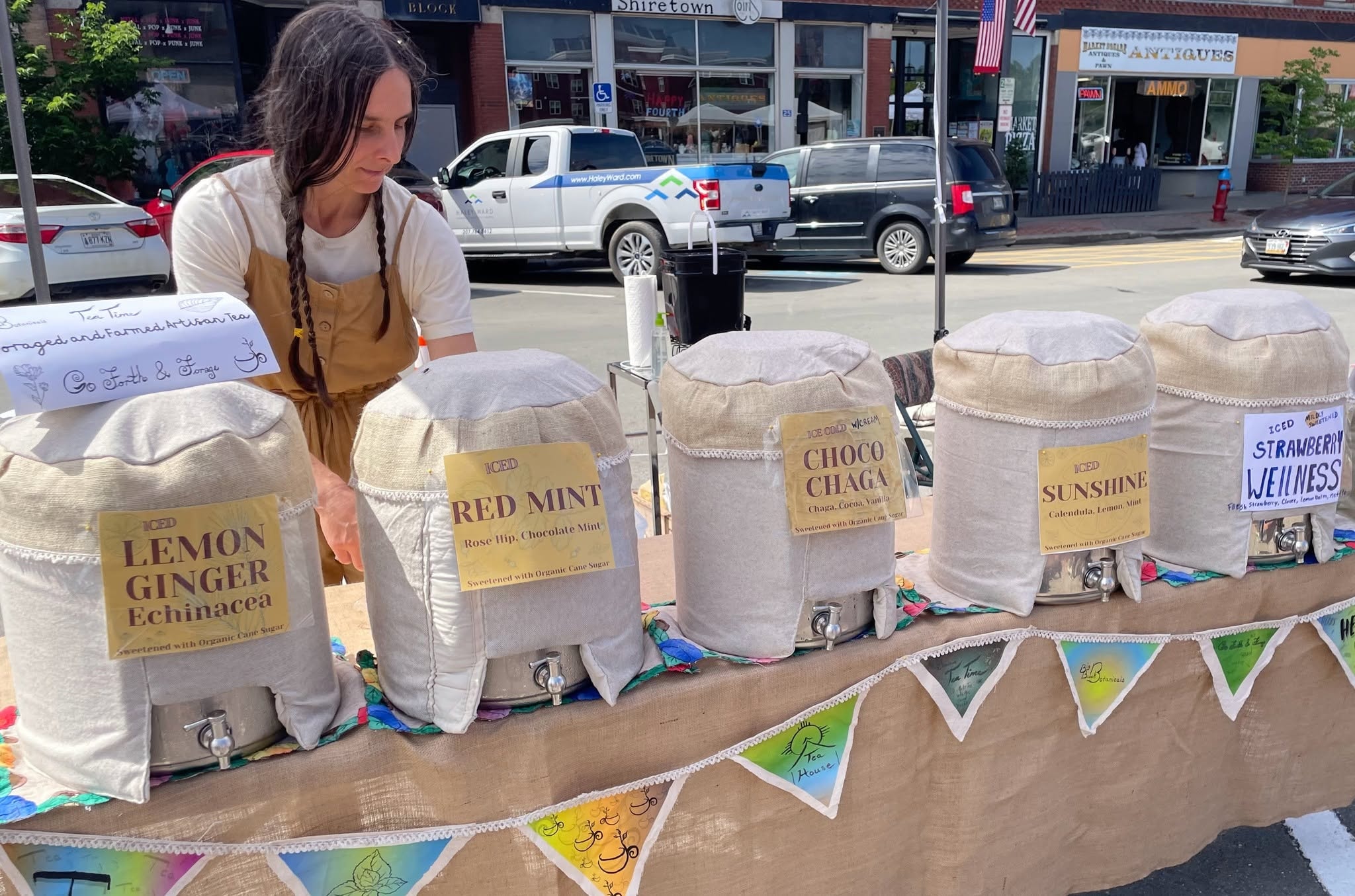 Big Brook Botanicals market booth with linen-wrapped iced tea dispensers at the Houlton Community Market