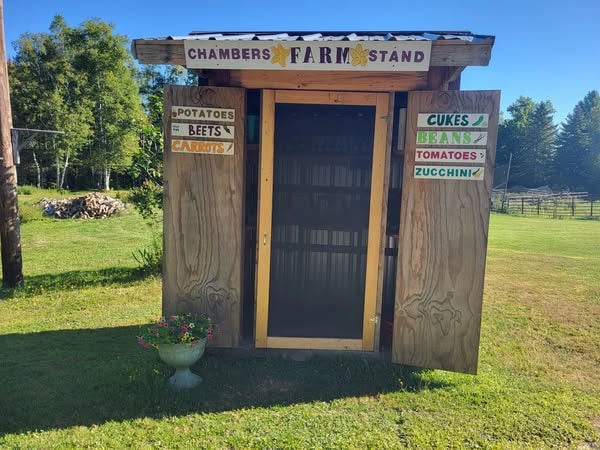 Chambers Farm Stand rustic wooden roadside stand with hand-painted signs for potatoes, beets, cukes, beans, tomatoes, and zucchini in Island Falls, Maine