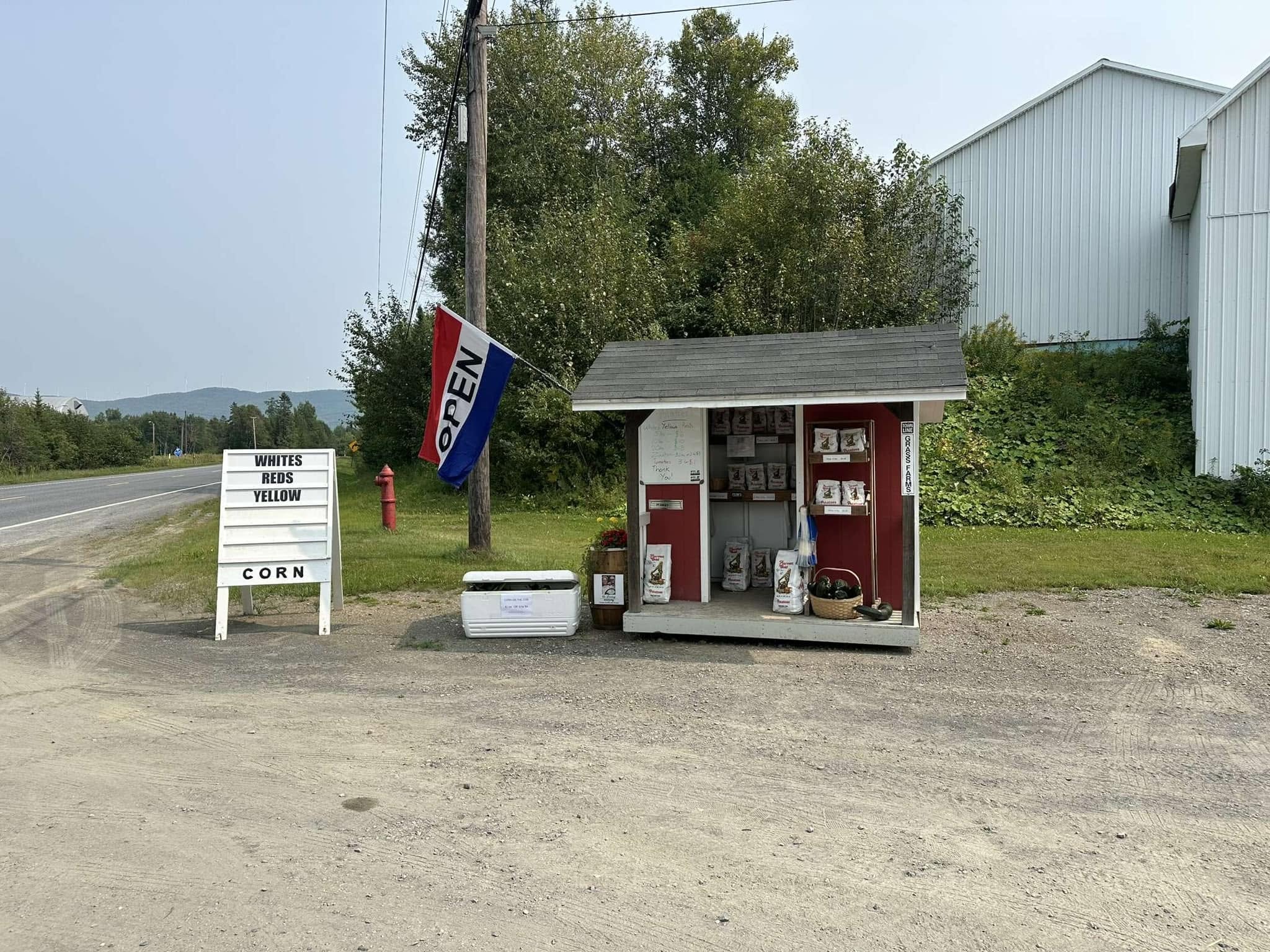 Grass Family Farm roadside stand with an open flag and fresh produce in Mars Hill, Maine
