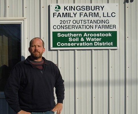 Shane Kingsbury standing beside the Kingsbury Family Farm conservation farmer sign