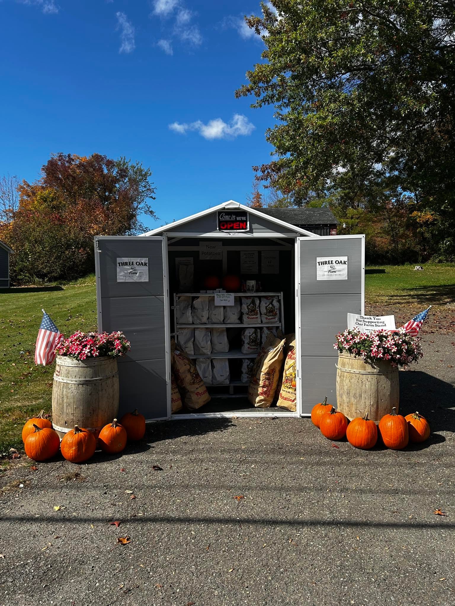 Qualey's Three Oak Farm Stand with potatoes, pumpkins, flowers, and open sign