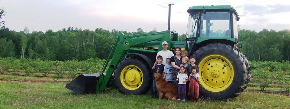 Sunnyside Farm family beside a green tractor in a cultivated field in Linneus, Maine